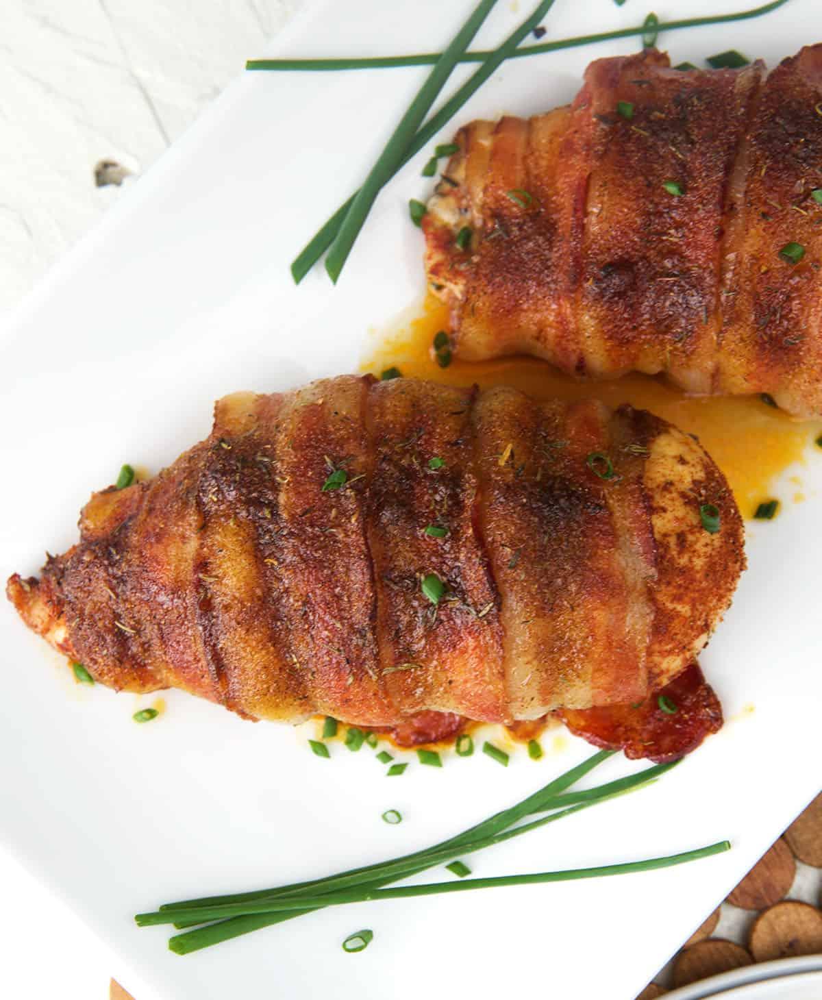 Petto di Pollo Avvolto nel Bacon 5 Petti di pollo cotti avvolti nella pancetta su un piatto bianco con erbe aromatiche.