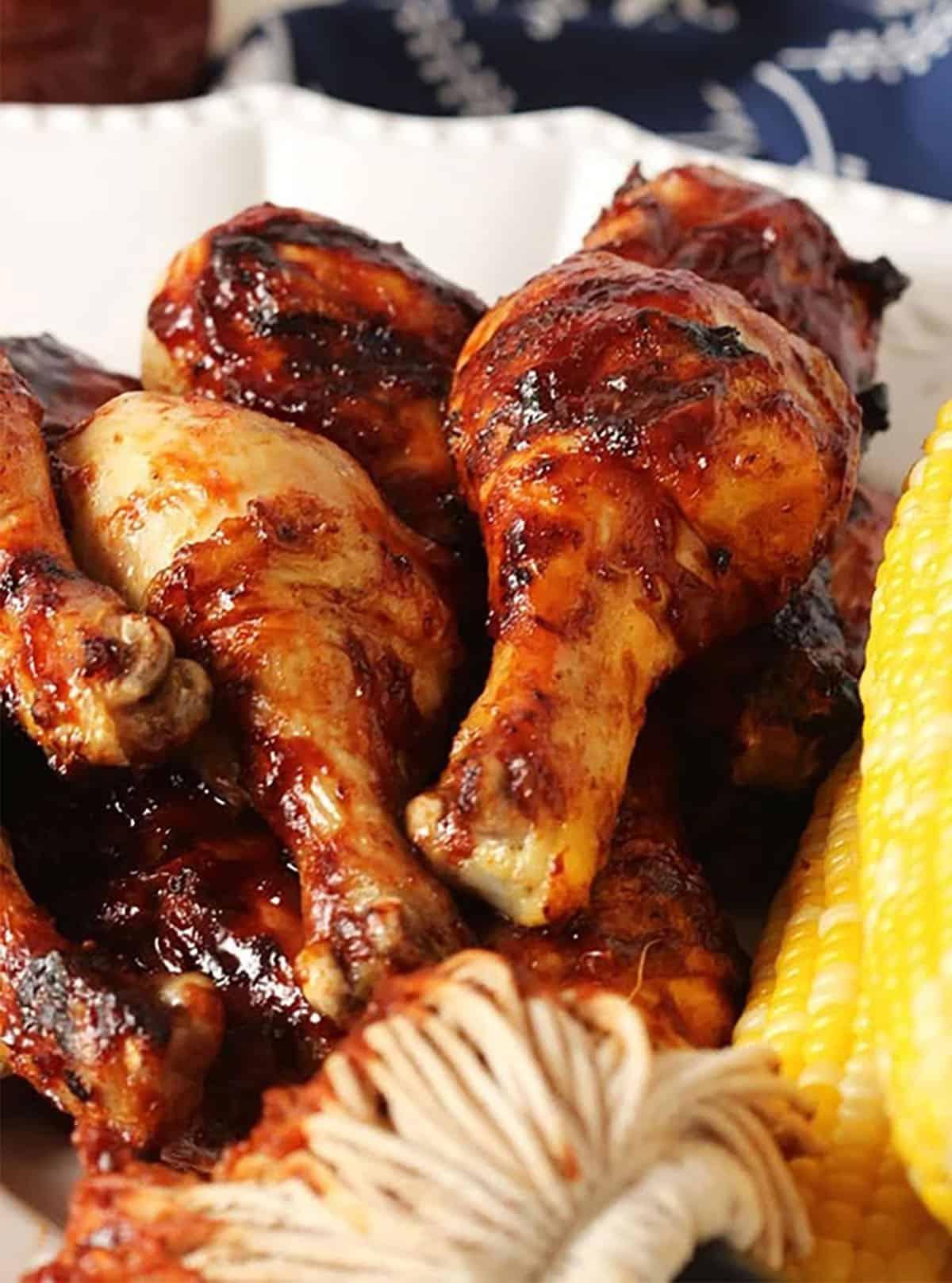 Cosce di Pollo al Barbecue 5 Cosce di pollo su un piatto con una spazzola da barbecue e pannocchie.