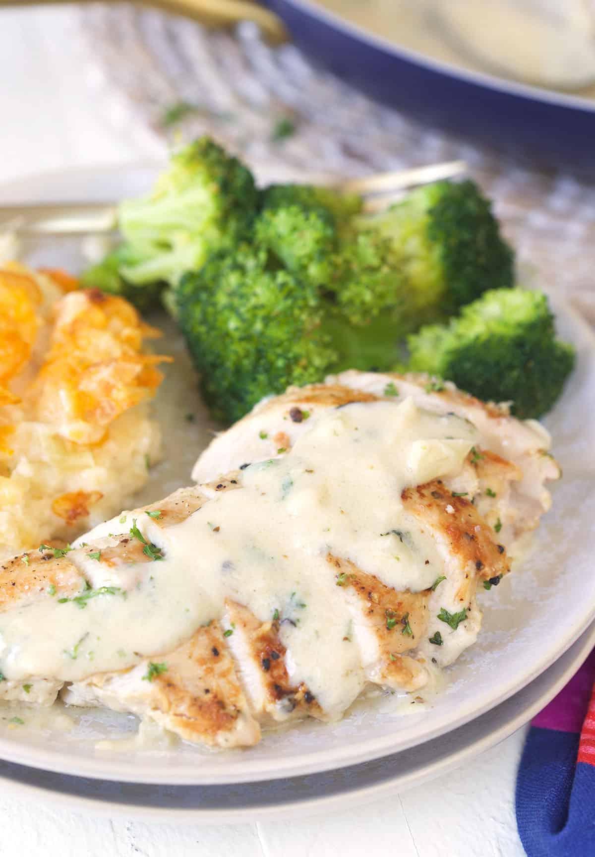 **Petto di Pollo Scottato in Padella con Salsa al Parmigiano e Aglio** 5 Broccoli e patate sono posizionati accanto a un petto di pollo coperto di salsa in un piatto.