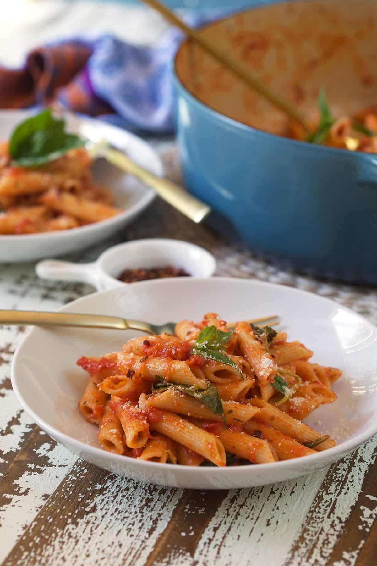 Penne al Pomodoro Veloce e Semplice 5 Un piatto bianco pieno di pasta al pomodoro e guarnito con basilico fresco.