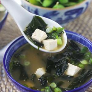 Zuppa di Miso Veloce e Facile 6 Un cucchiaio bianco solleva una porzione di zuppa dalla ciotola, con il vapore che sale.