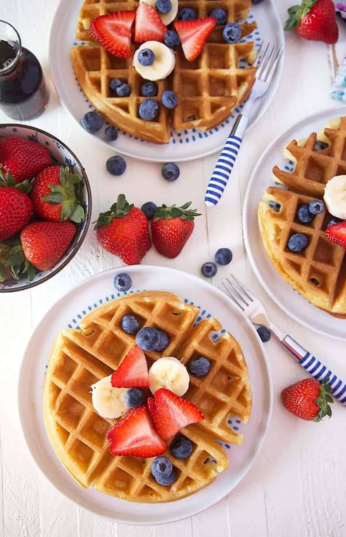 Il Migliore Waffle Belga Casalingo 6 Waffles belgi con frutta fresca e panna montata su uno sfondo bianco, vista dall'alto.