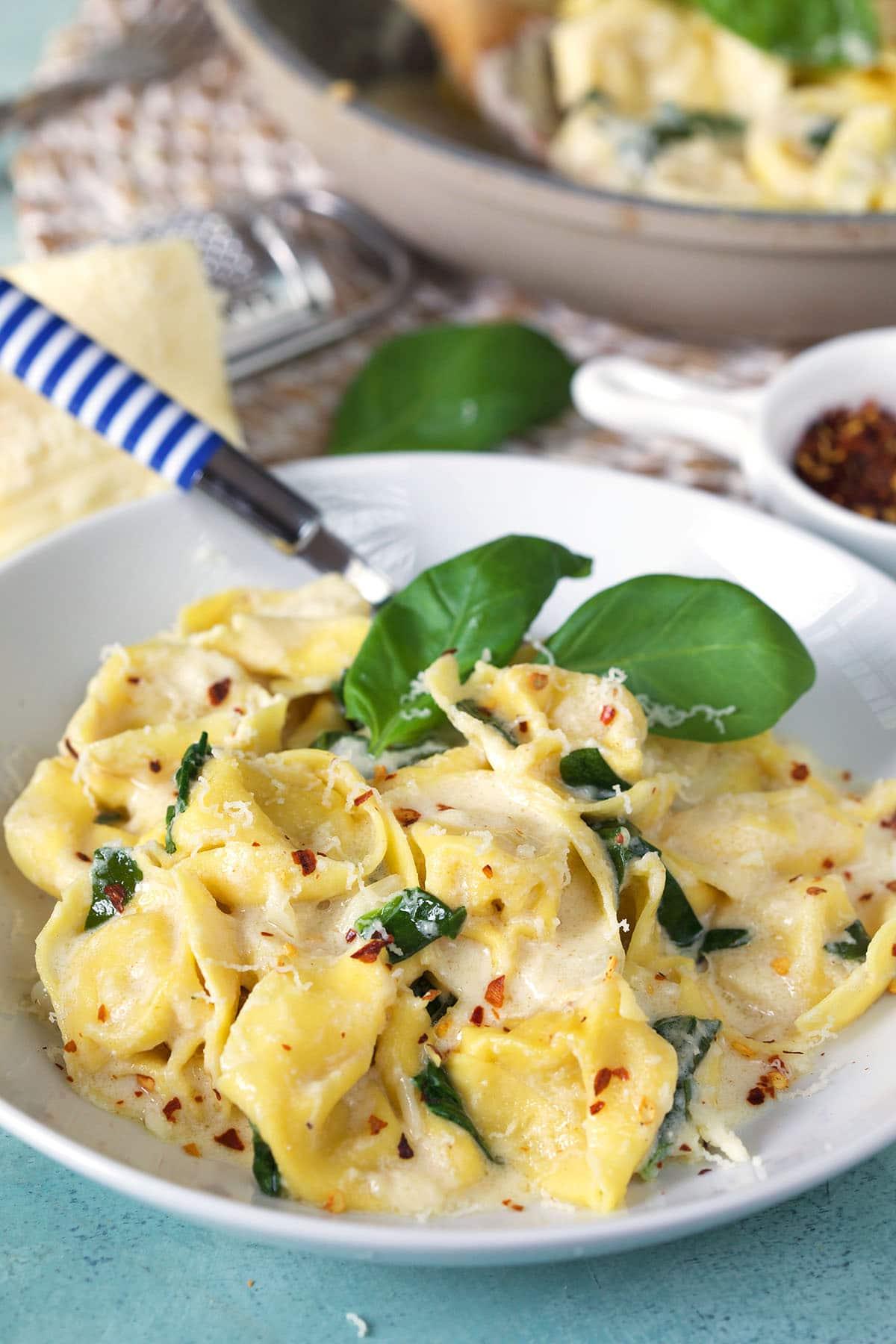 Tortellini all'Asiago 6 Un piatto di tortellini in salsa è guarnito con basilico fresco, pronto per essere servito.