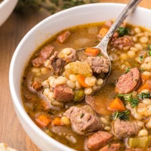 Zuppa di Manzo e Orzo con Salsiccia Andouille 6 Un cucchiaio sta immergendo in una ciotola piena di zuppa.