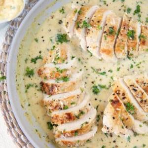 **Petto di Pollo Scottato in Padella con Salsa al Parmigiano e Aglio** 6 Diversi petti di pollo affettati sono ricoperti di salsa bianca in una padella.