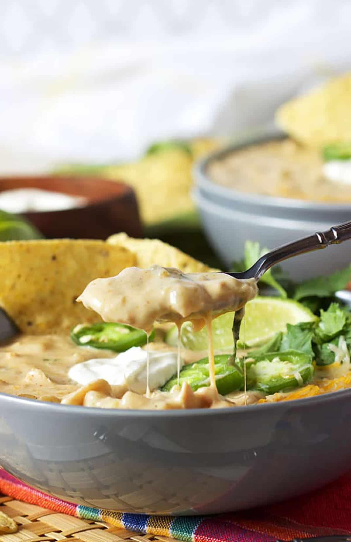 Il Miglior Chili Bianco Cremoso di Pollo 6 Un cucchiaio di chili di pollo viene prelevato da una ciotola.