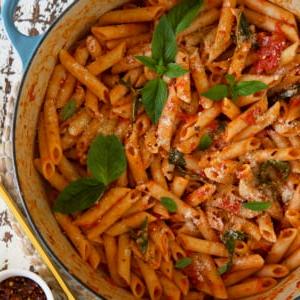 Penne al Pomodoro Veloce e Semplice 6 Una pentola in ghisa bianca e blu piena di penne al pomodoro cotte, guarnite con basilico fresco.