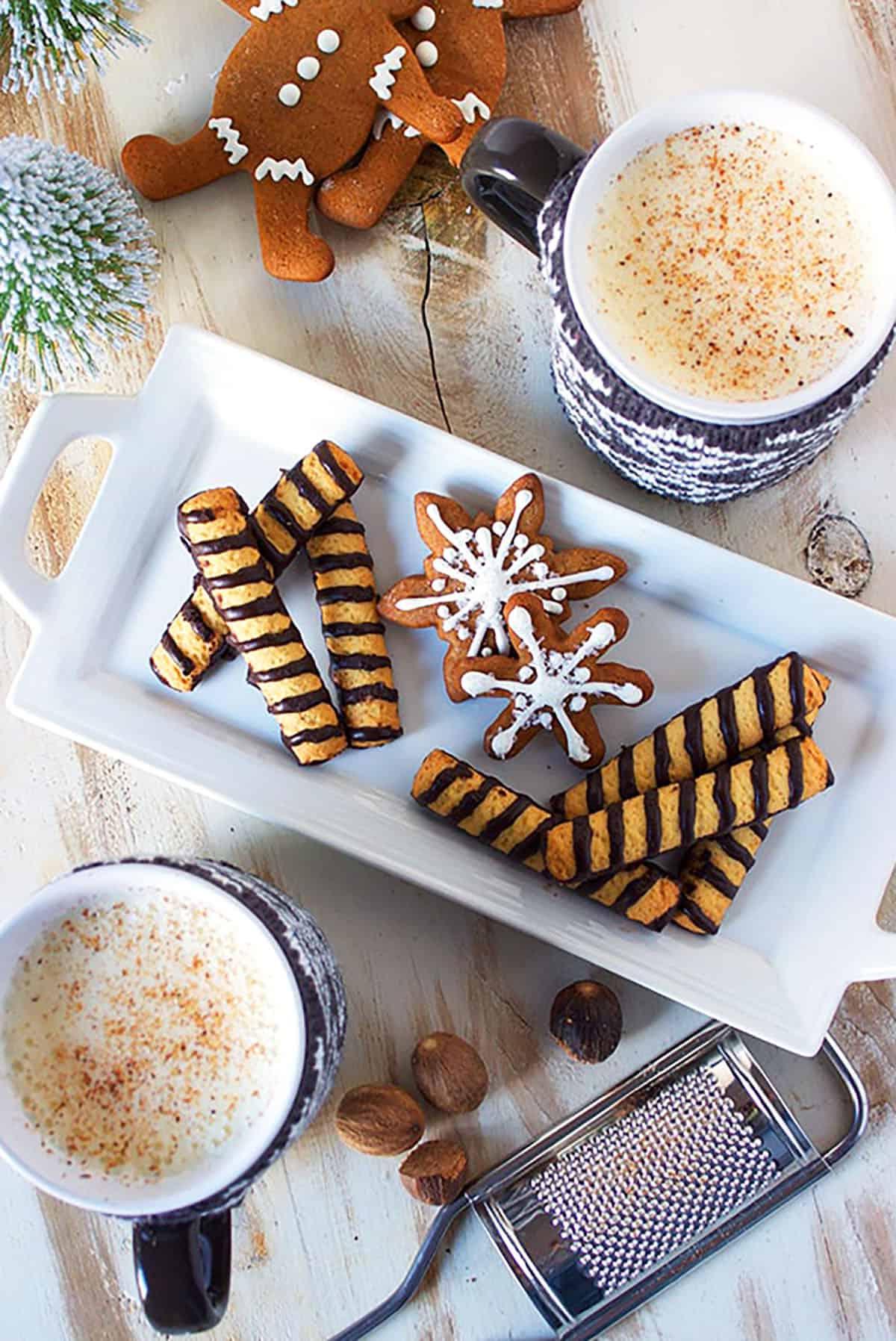 La Migliore Ricetta Fatta in Casa di Zabaione 6 Piatto rettangolare bianco con biscotti natalizi e due tazze di eggnog.