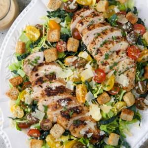 Insalata Caesar con Pollo 6 Un grande piatto da portata bianco è sormontato da insalata Caesar con pollo.