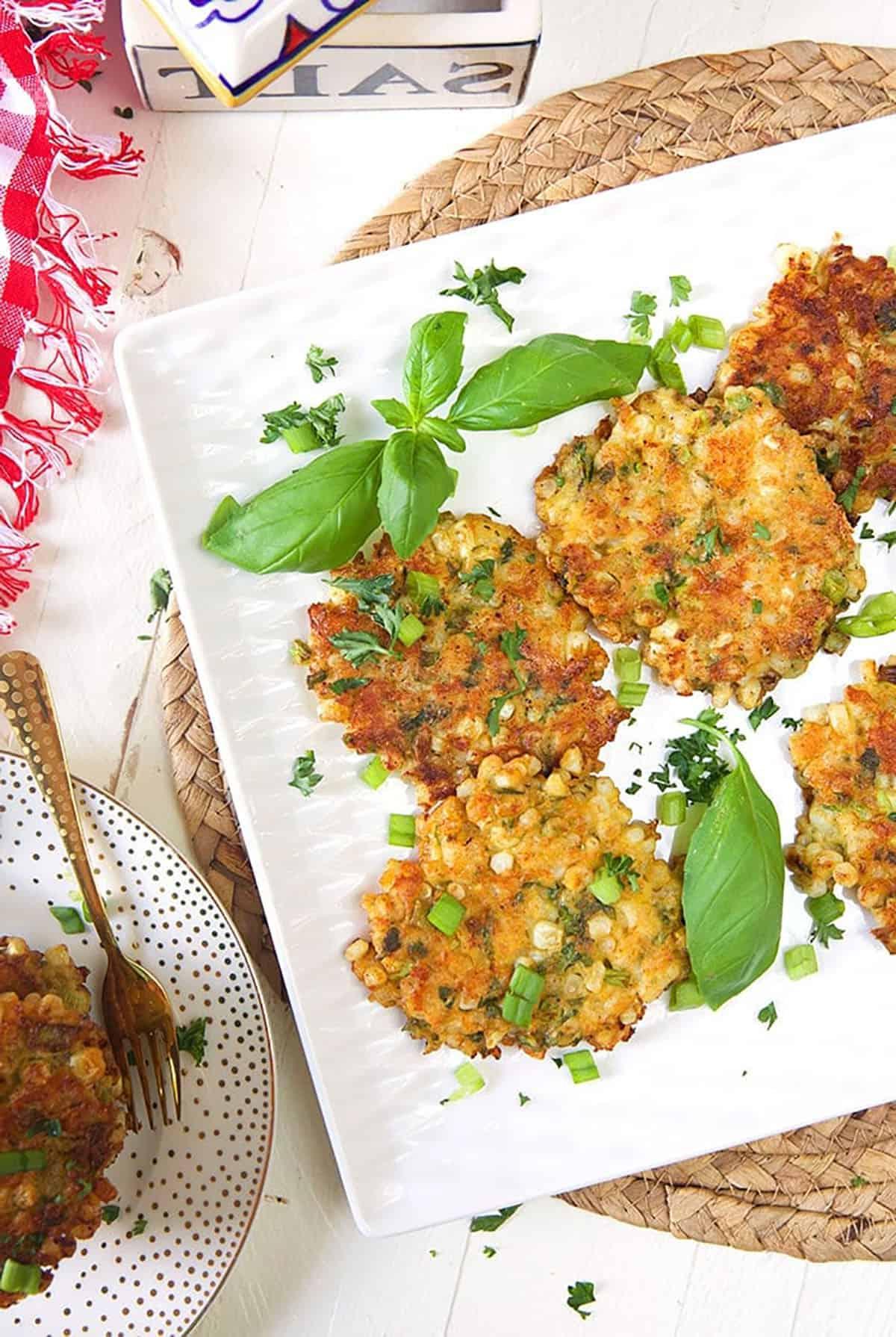 Frittelle di Mais all'Antica con Cheddar e Basilico 6 Ripresa dall'alto di frittelle di mais su un piatto quadrato bianco con un tovagliolo a quadri rossi e bianchi.