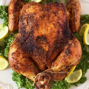 Come preparare il Pollo allo Spiedo 6 Un pollo arrosto intero su un piatto bianco con guarnizioni di prezzemolo e fette di limone.