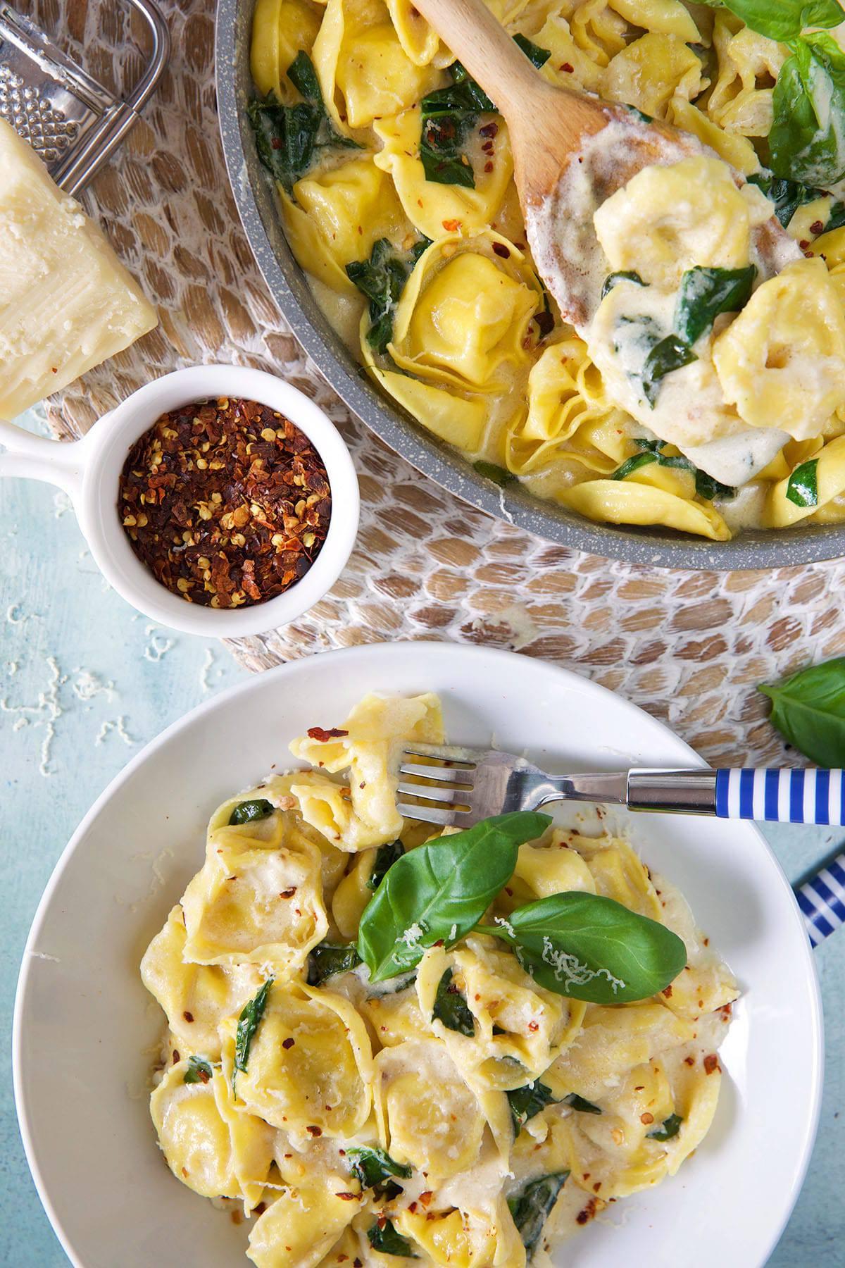 Tortellini all'Asiago 7 Una porzione di tortellini è presentata accanto a una tazza di peperoncino tritato e una casseruola piena.