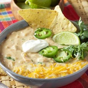 Il Miglior Chili Bianco Cremoso di Pollo 7 chili bianco di pollo in una ciotola grigia con patatine e jalapeño sopra. Ciotola di lime sullo sfondo.