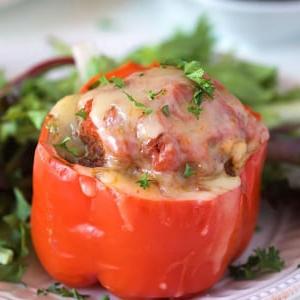Ricetta Peperoni Ripieni Instant Pot 8 Peperone rosso ripieno ricoperto di formaggio su un piatto bianco con verdure.