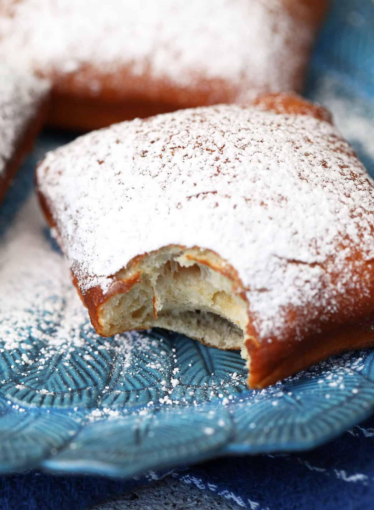 Facili Bignè di New Orleans 8 Primo piano di un beignet su un piatto con un angolo morso per mostrare la consistenza soffice