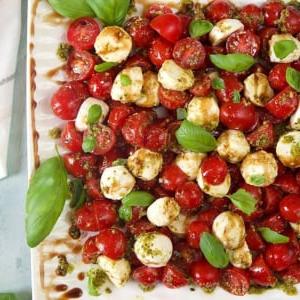 Insalata di Pomodoro e Mozzarella 8 Insalata Caprese con pomodorini su un piatto bianco, guarnita con foglie di basilico, vista dall'alto.