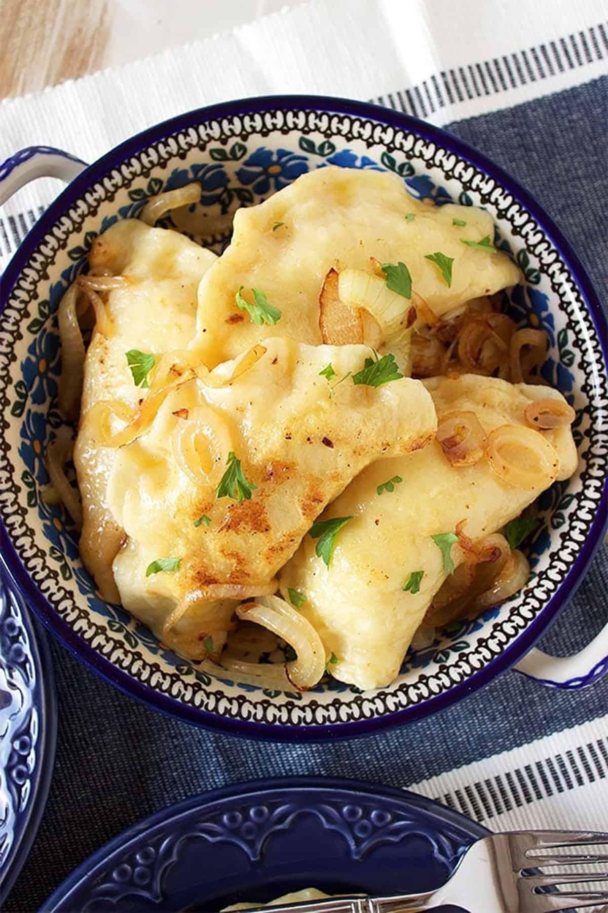 La migliore ricetta di pierogi di patate 8 Quattro pierogi di patate in una pirofila di ceramica polacca su una tovaglietta blu.
