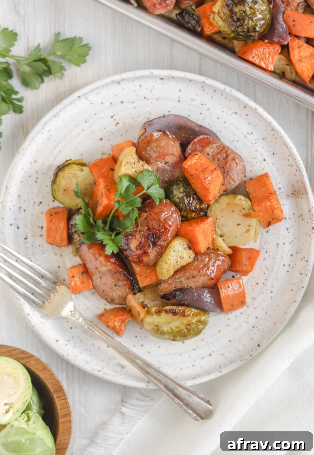 Chicken sausage with roasted veggies on a round white plate topped with parsley with a vintage fork on the plate.