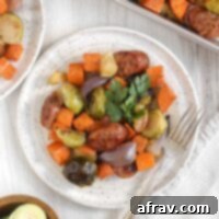 Chicken sausage with roasted veggies on a round white plate topped with parsley with a vintage fork on the plate.