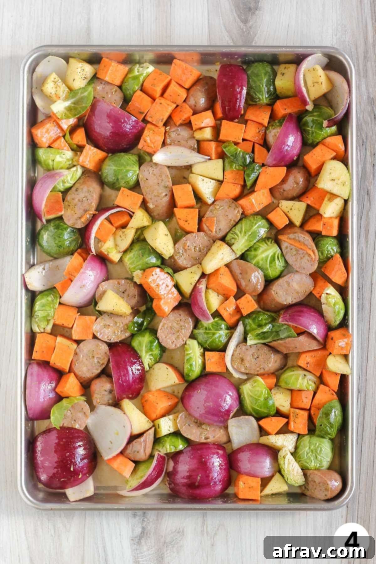 Sliced chicken sausage, chopped vegetables, and chopped apple on a large baking sheet before being cooked.