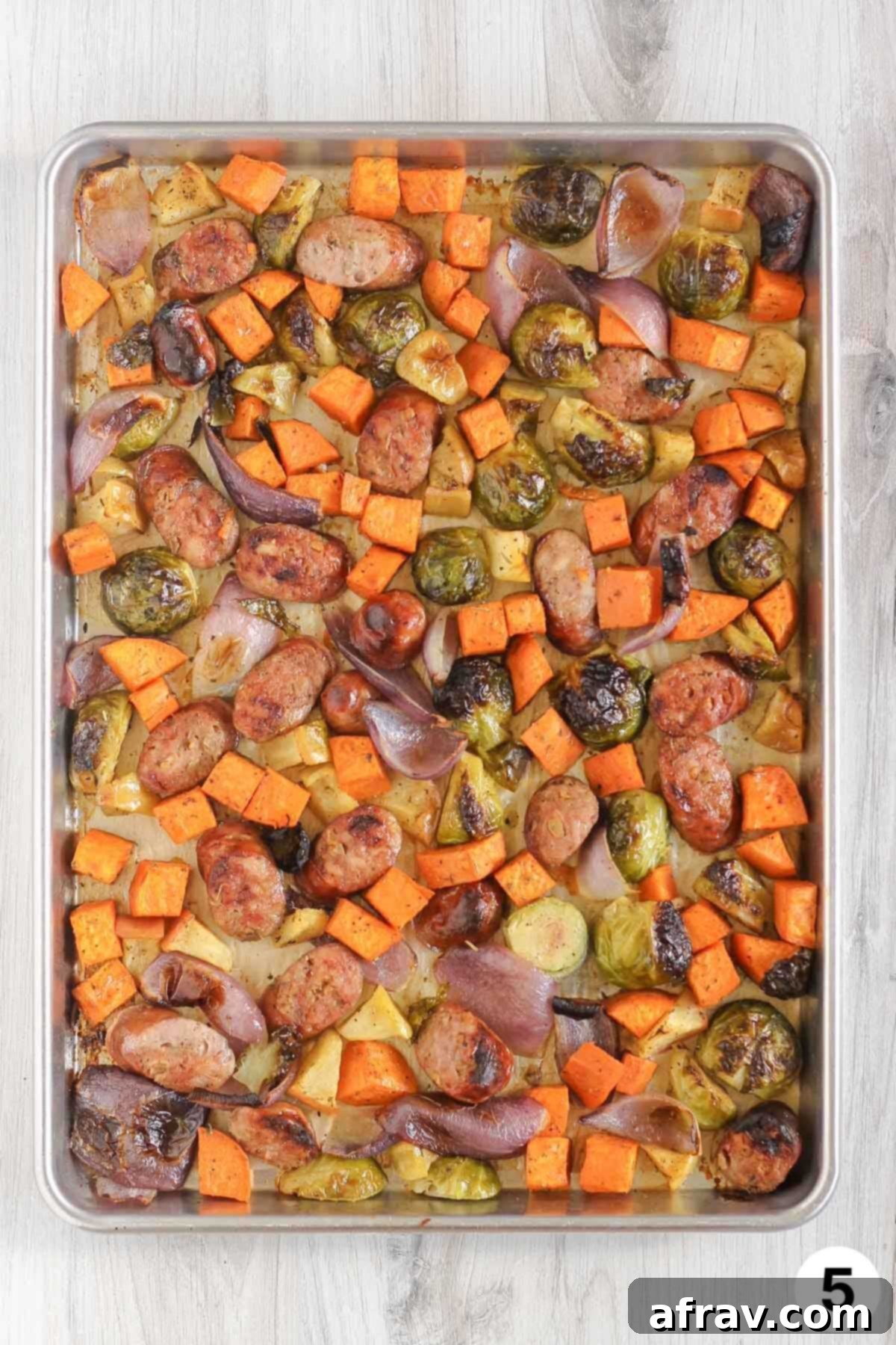 Roasted vegetables, apples, and chicken sausage on a large baking sheet.