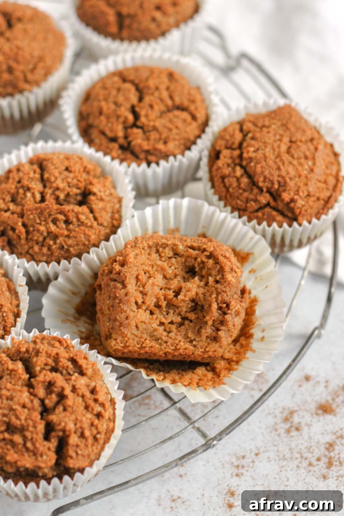 Paleo pumpkin muffins on a round wire cooling rack with a bite taken out of the center muffin laying in a white paper muffin liner.