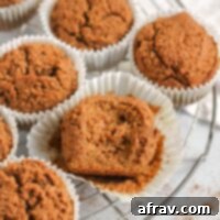 Paleo pumpkin muffins on a round wire cooling rack with a bite taken out of the center muffin laying in a white paper muffin liner.