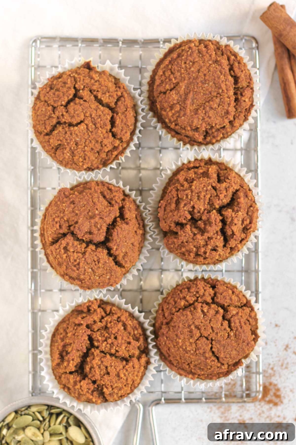 Pumpkin muffins on a rectangular wire rack with cinnamon sticks and pumpkin seeds off to the side.