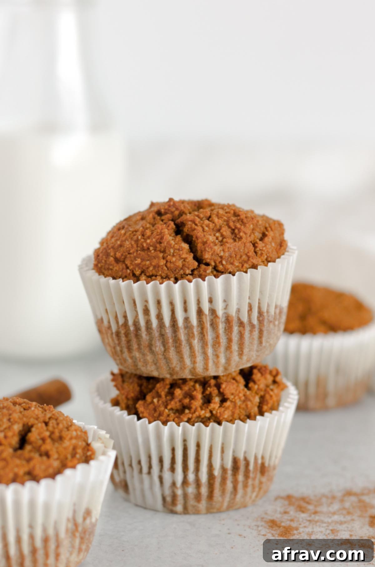 Paleo pumpkin muffins stacked two high with a jar of milk and additional muffins in the background.