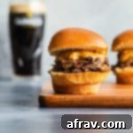 Side view of a Guinness braised beef slider on a wooden board with a glass of Guinness in the background.