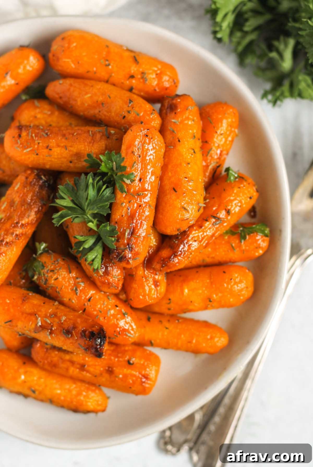 Roasted baby carrots sprinkled parsley on a small plate with vintage forks laying next to the plate.
