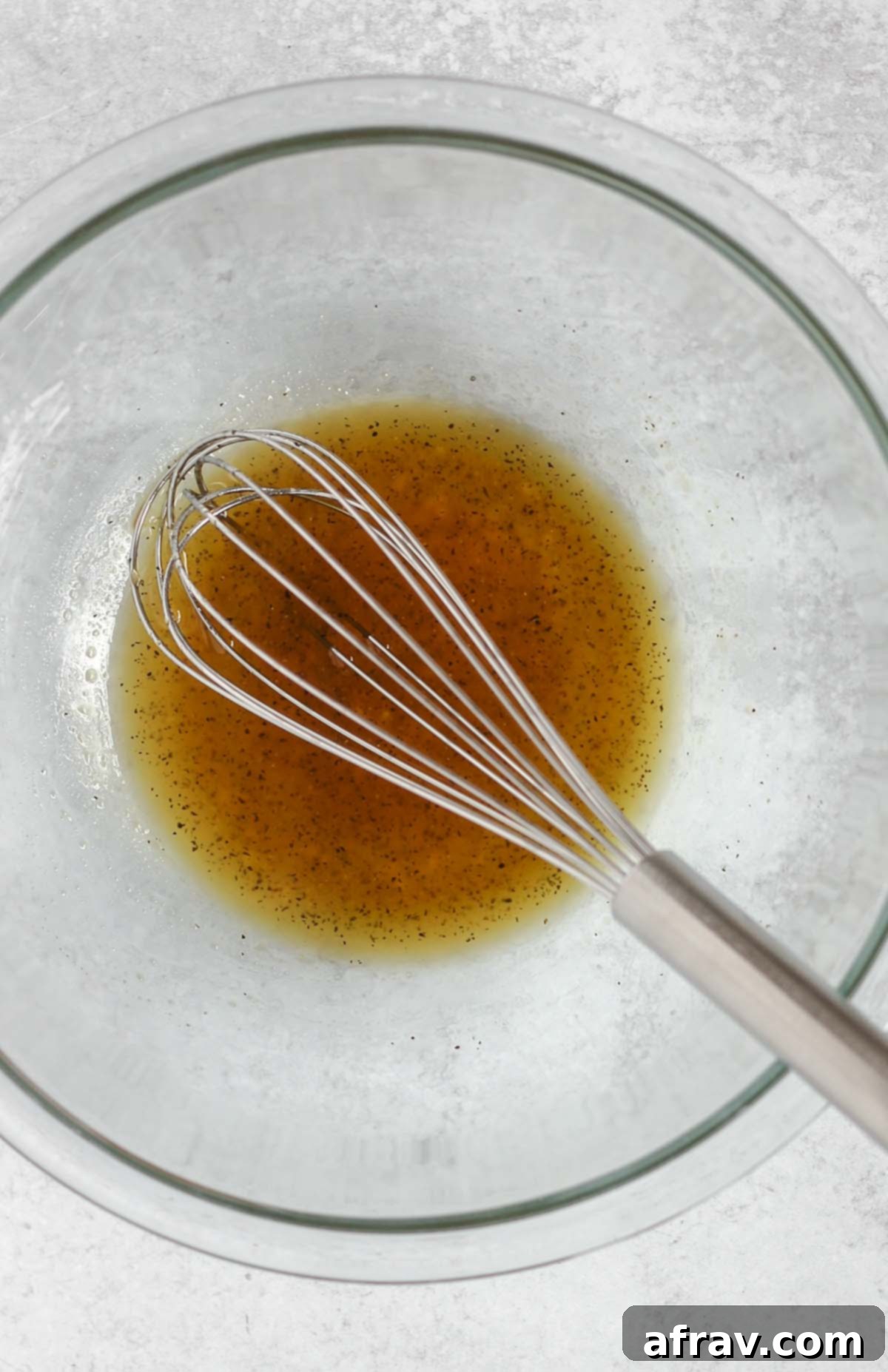 Wire whisk mixing honey marinade in a small glass mixing bowl.