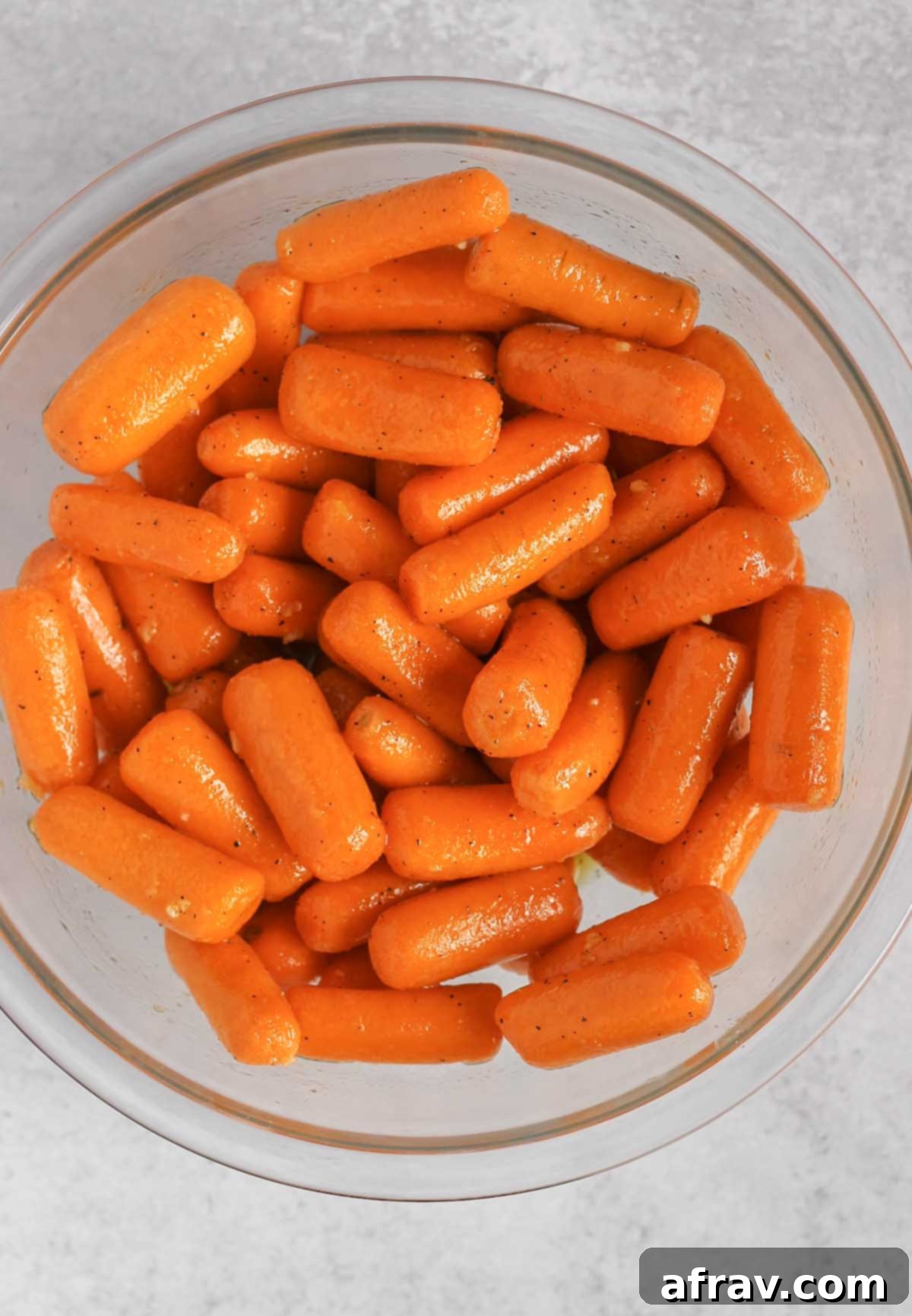 Baby carrots mixed with honey marinade in a glass mixing bowl.