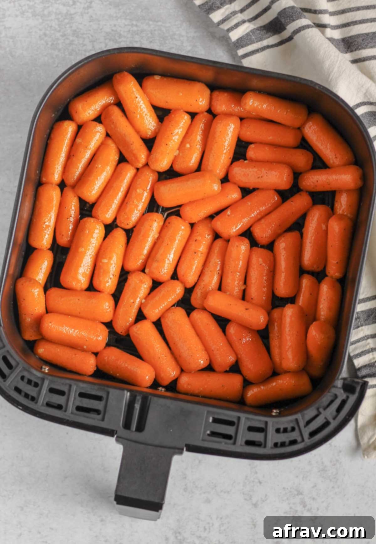 Raw baby carrots coated in a honey glaze in an air fryer basket.