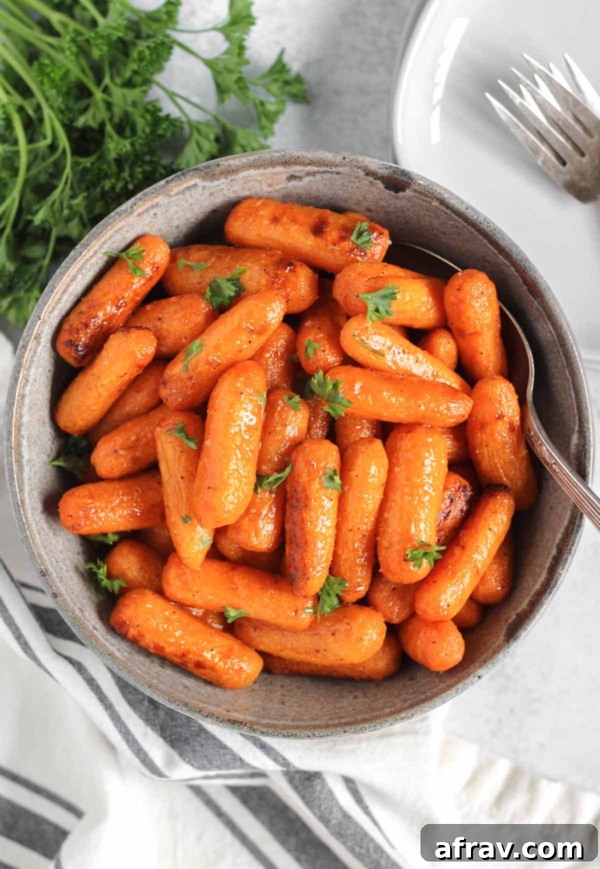 Air fried roasted baby carrots sprinkled with parsley in a gray serving bowl with a spoon.