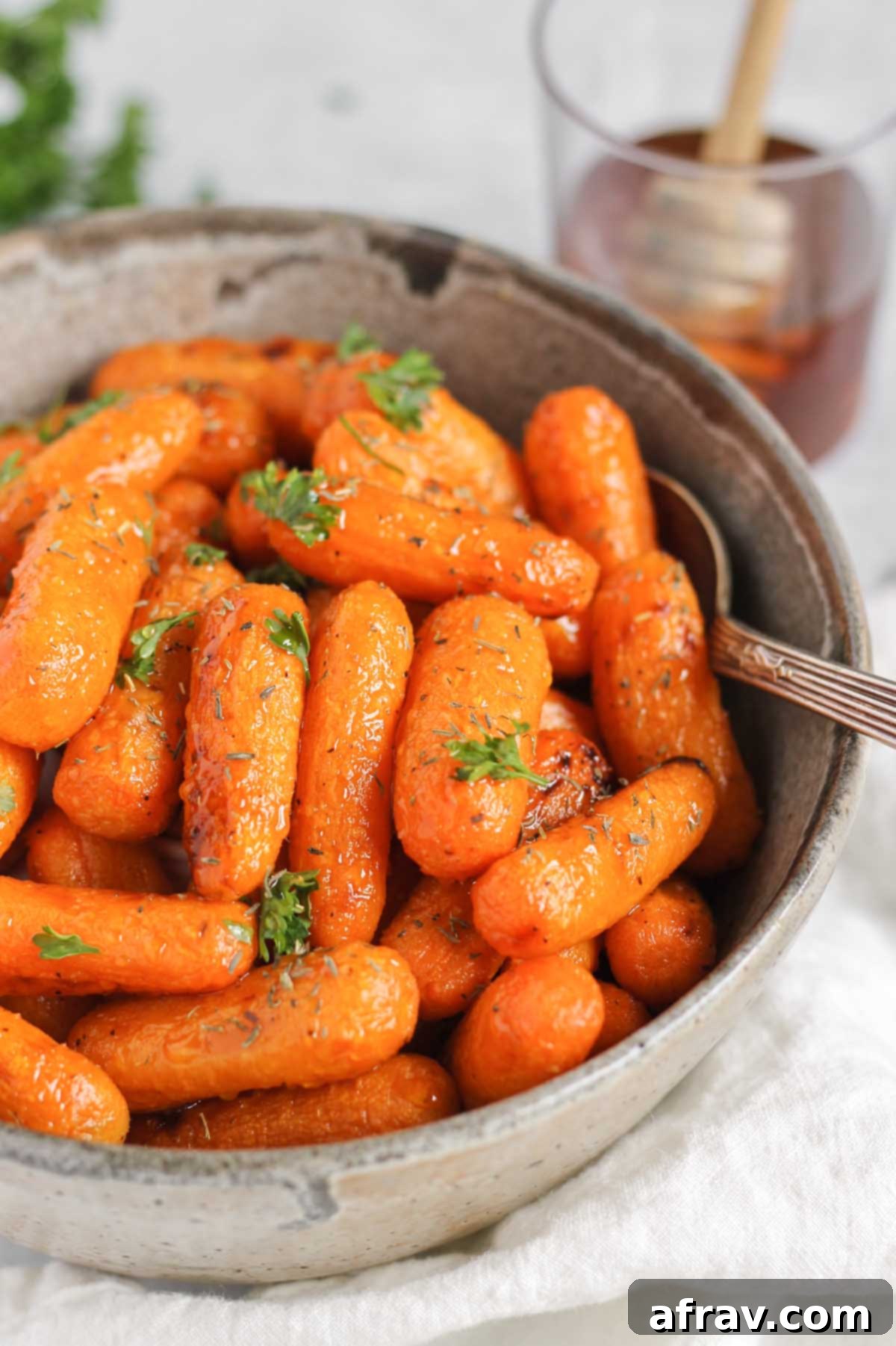 Air fryer roasted baby carrots in a gray serving bowl with a cup of honey in the back ground.