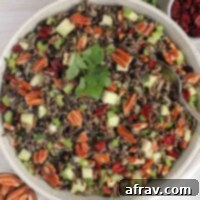 Wild rice salad with pecans, dried cranberries, and apples in a ceramic serving bowl with a vintage serving spoon in the salad.