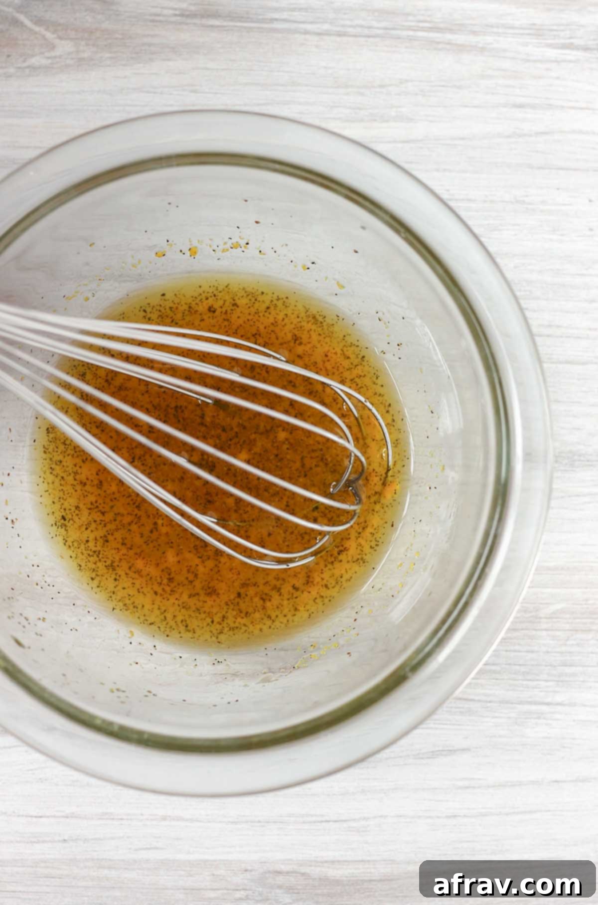 Orange vinaigrette dressing in a mixing bowl with a whisk.