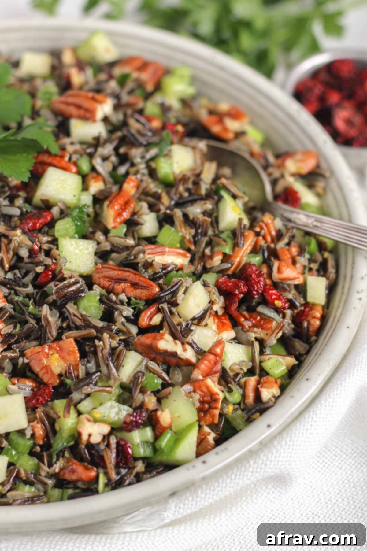 Cold wild rice salad with a vintage serving spoon in a ceramic serving bowl.