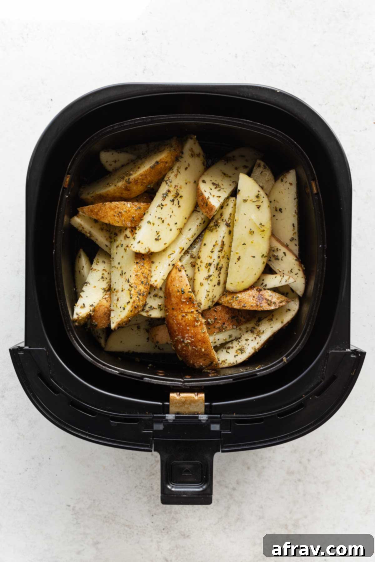 Overhead view of seasoned raw potato wedges in an air fryer basket.