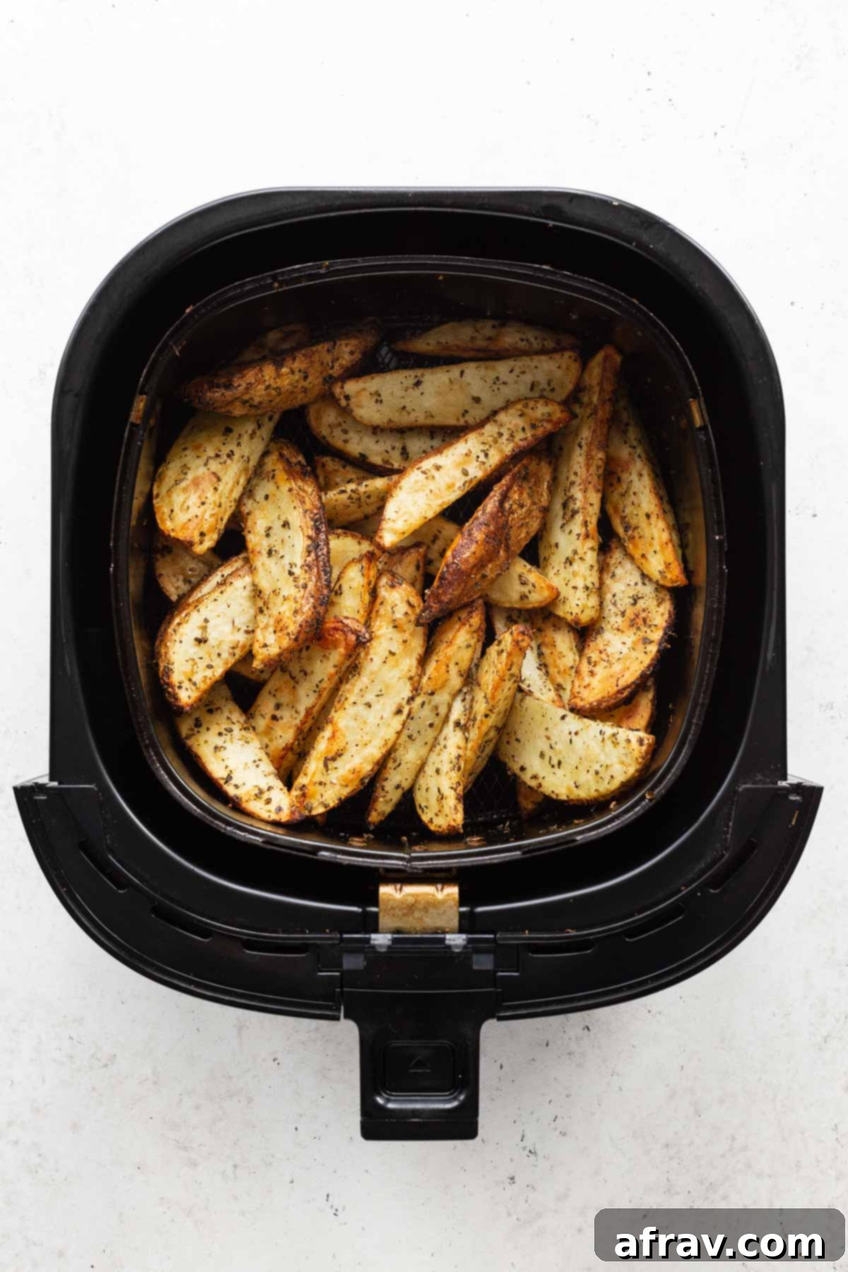 Overhead view of air fried potato wedges in an air fryer basket.