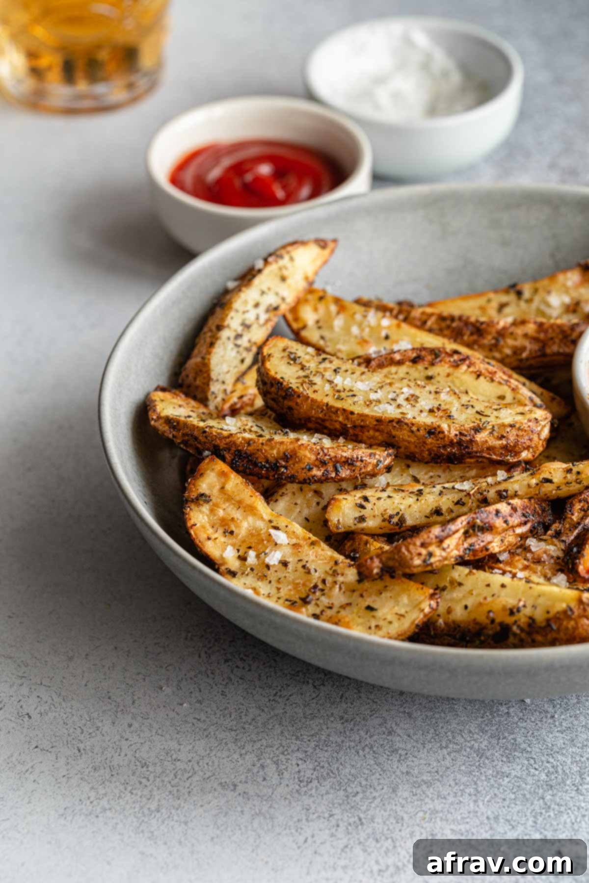 Side view of wedge fries in a grey bowl with ketchup in the background.