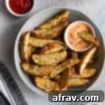 Overhead view of air fryer potato wedges in a grey bowl with dipping sauces off to the sides.