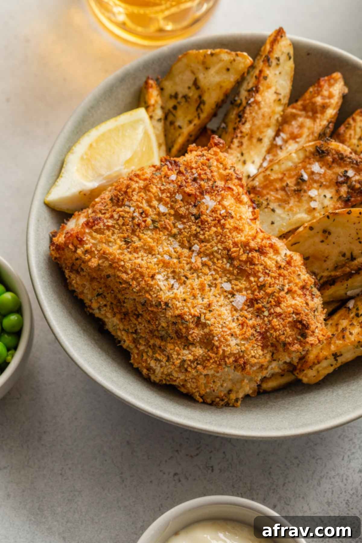Close up of crispy breaded cod in a bowl with wedge fries.