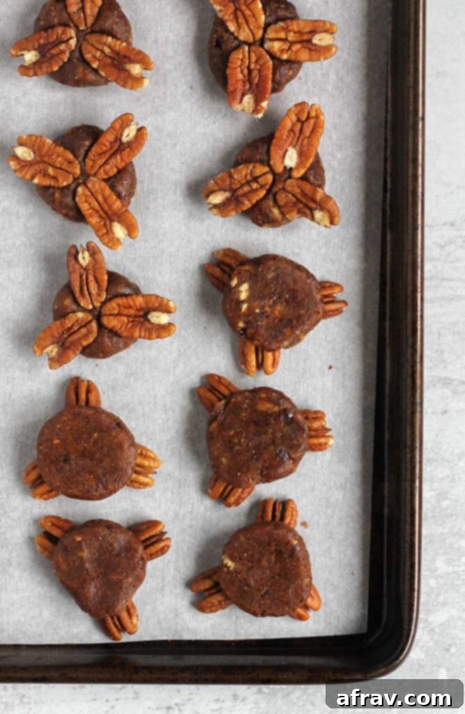 Date balls with 3 pecans smashed into them on a baking sheet.