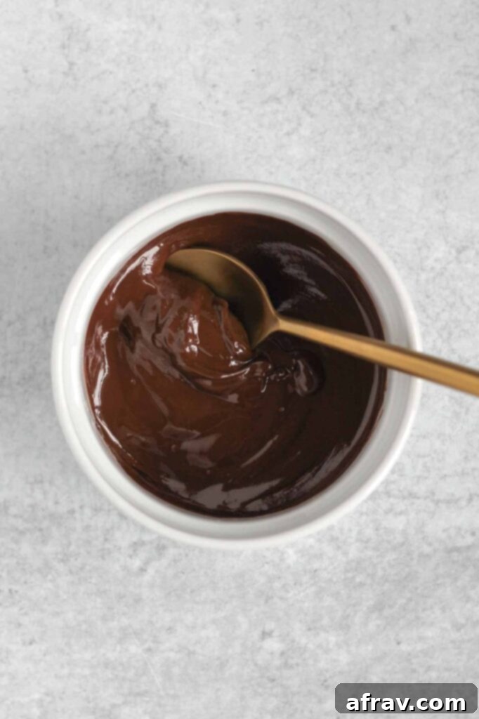 Melted chocolate in a small white bowl with a gold spoon.