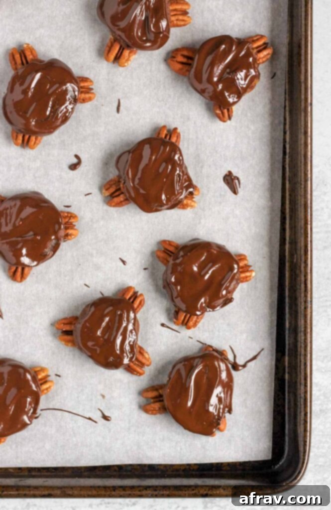 Turtle candies with melted chocolate spread on top on a parchment lined baking sheet.