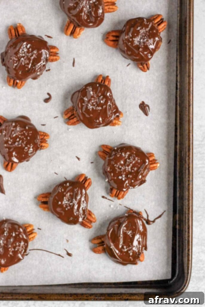 Vegan chocolate turtles spread with melted chocolate and topped with sea salt on a baking sheet that's been lined with parchment paper.