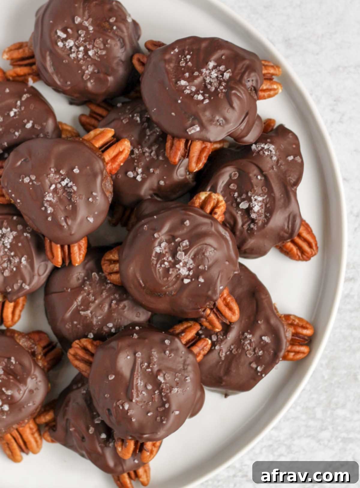 Vegan chocolate turtles sprinkled with sea salt on a round white plate.