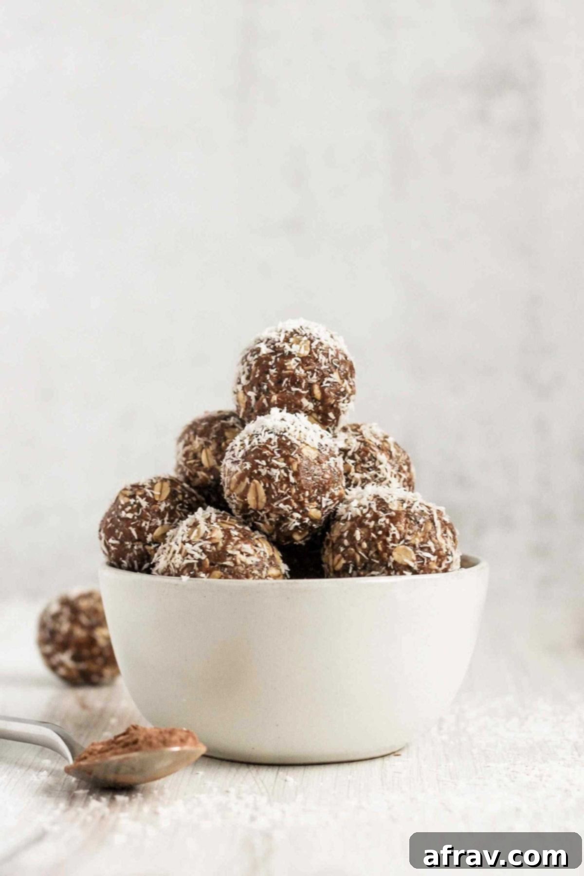 Chocolate Coconut Peanut Butter Balls 2 Chocolate peanut butter energy balls sprinkled with coconut flakes, neatly stacked in a small white bowl.